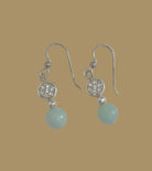 Pair of earrings with green beads and silver accents on a light gray background